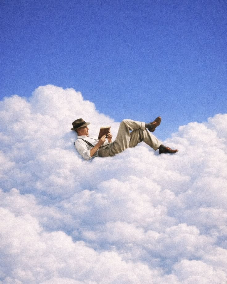 A man in a hat lying on a cloud, reading a book against a blue sky